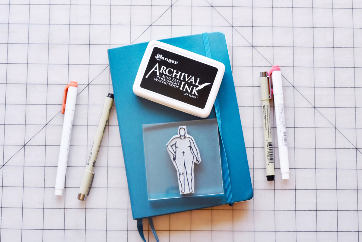 A custom rubber stamp of my body model croquis! Shown here with my sewing bujo key supplies: blue bullet journal, ink pad, pens and markers, along with my new custom body positive fashion croquis stamp.
