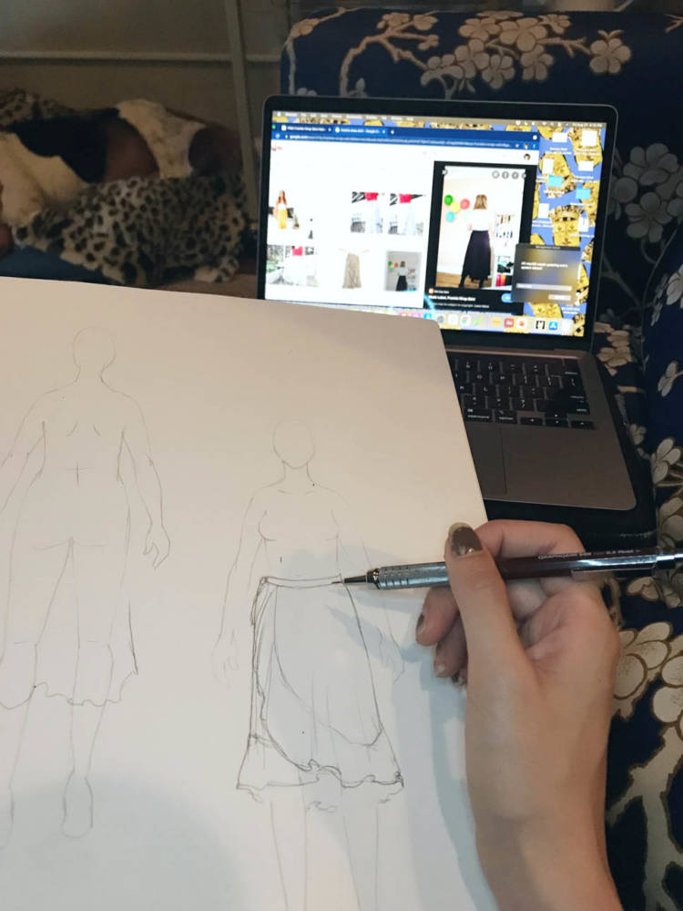 Amanda sketches a shirt over her MyBodyModel croquis as she looks at an image of the skirt pattern on her laptop in the distance for reference. 