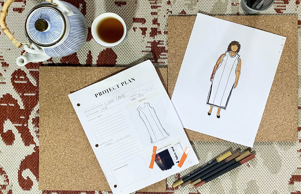 A spread of Tiffaney's MyBodyModel paper doll croquis wearing a paper garment version of the Lane dress from Seamwork alongside a teapot and cup of tea, several colored markers, and a sheet for sewing project plans.