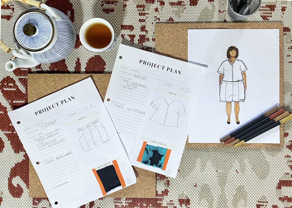 A spread of Tiffaney's MyBodyModel paper doll croquis wearing a paper garment version of the Marlow shirt and Dorian shorts from Seamwork alongside a teapot and cup of tea, several colored markers, and two sheets for project plans.